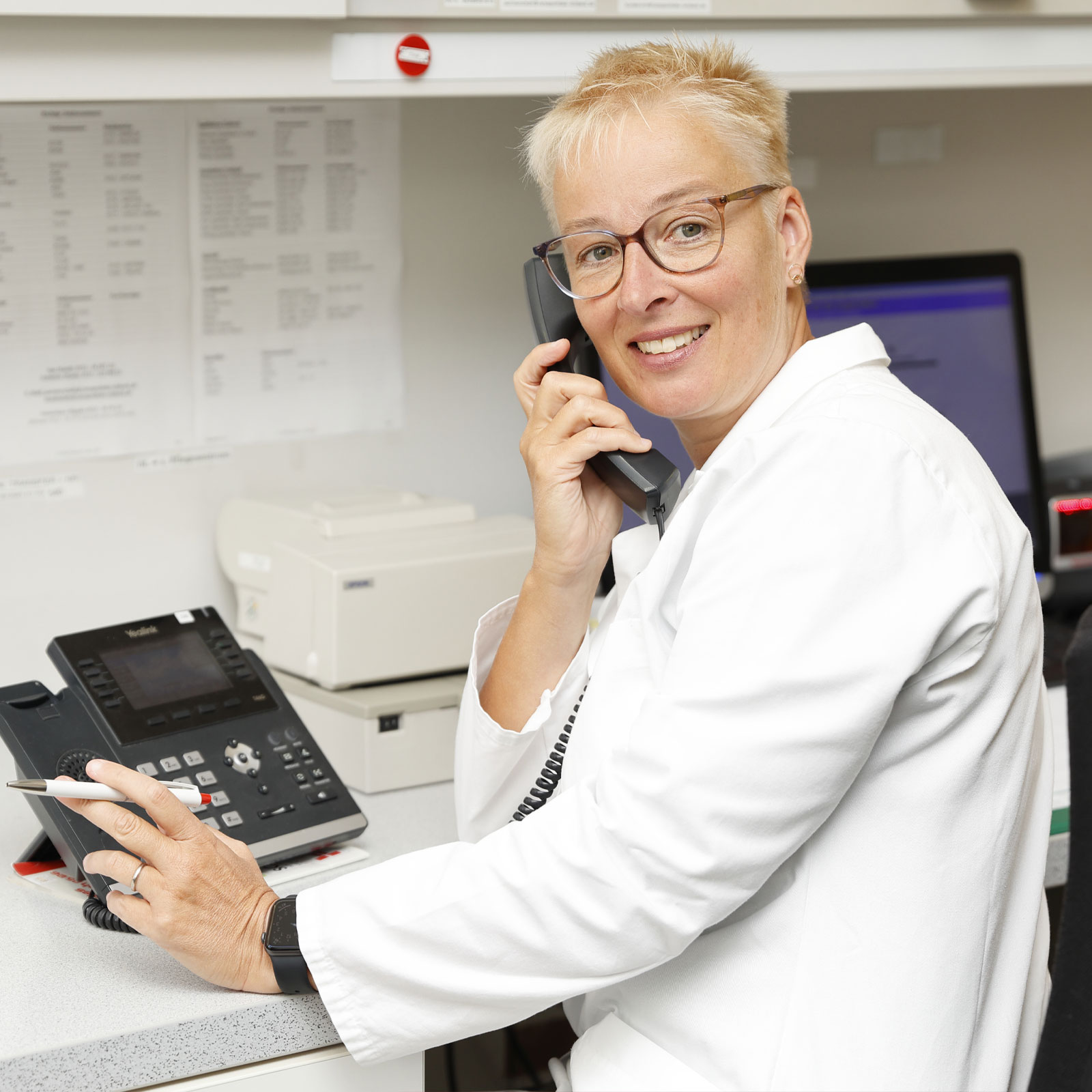 Eine lächelnde Apothekerin hält einen Telefonhörer und berät am Telefon.