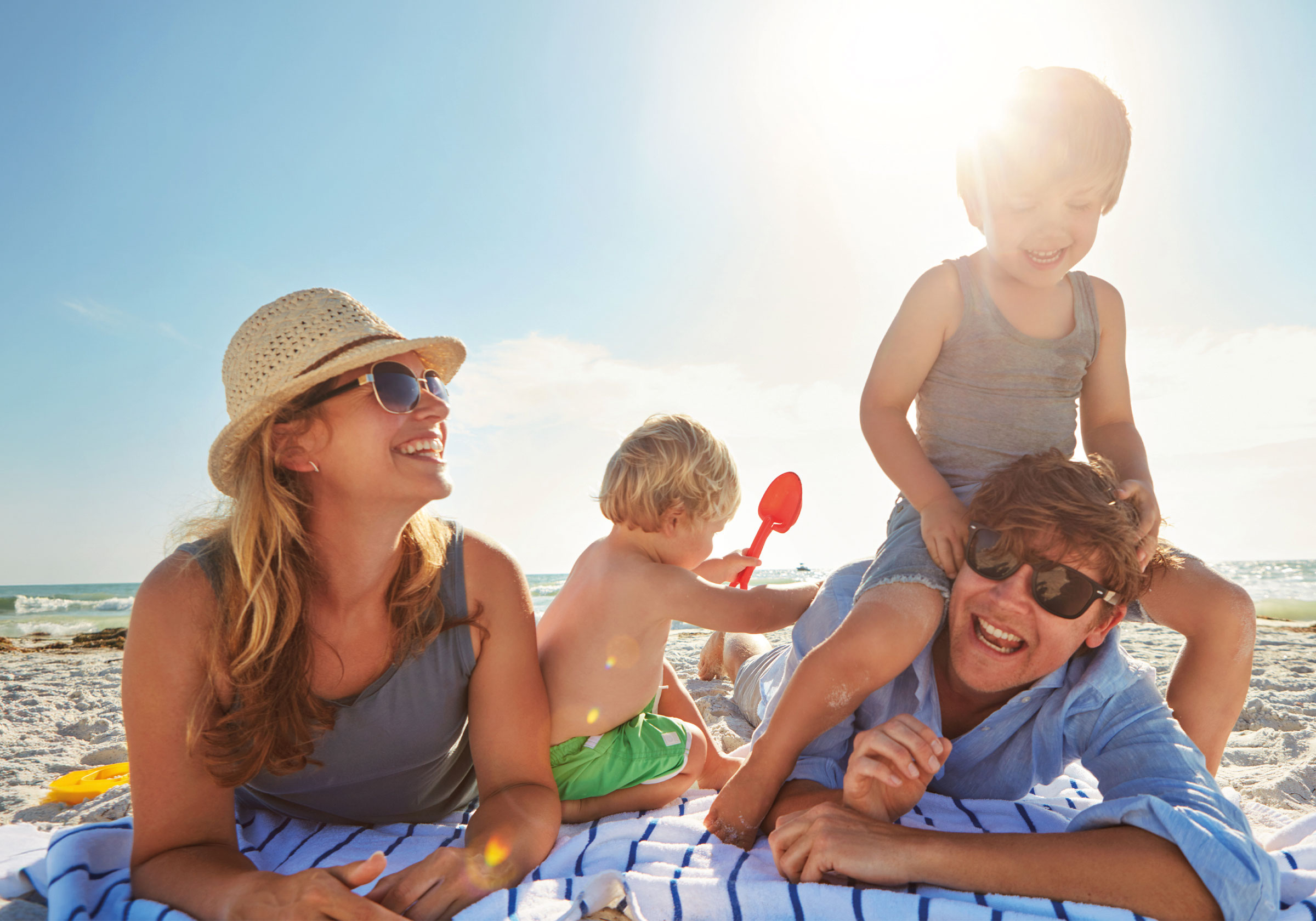 Zwei Erwachsene und zwei Kinder liegen lachend am Strand, helles Sonnenlicht